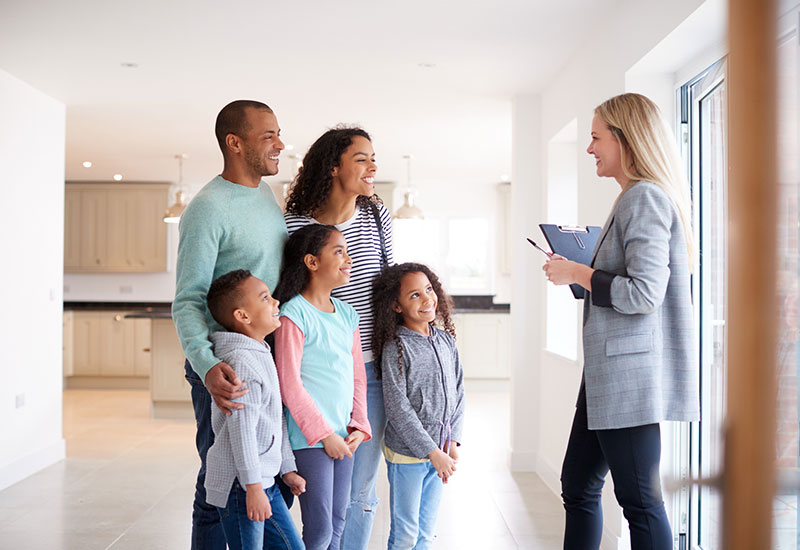 Female Real Estate Agent Showing Family Interested In Buying Around House